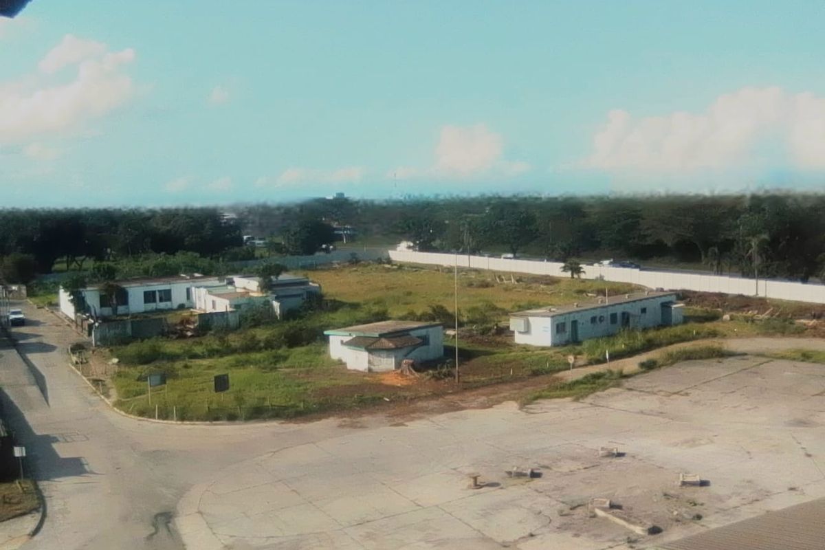 An elevated aerial view of an industrial site featuring multiple detached structures, expansive paved areas, and surrounding undeveloped land.