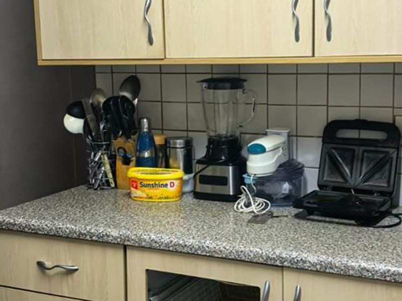 A kitchen section featuring light wood-tone cabinetry, a granite-look countertop, and a tiled backsplash, currently showing a missing cabinet door panel.