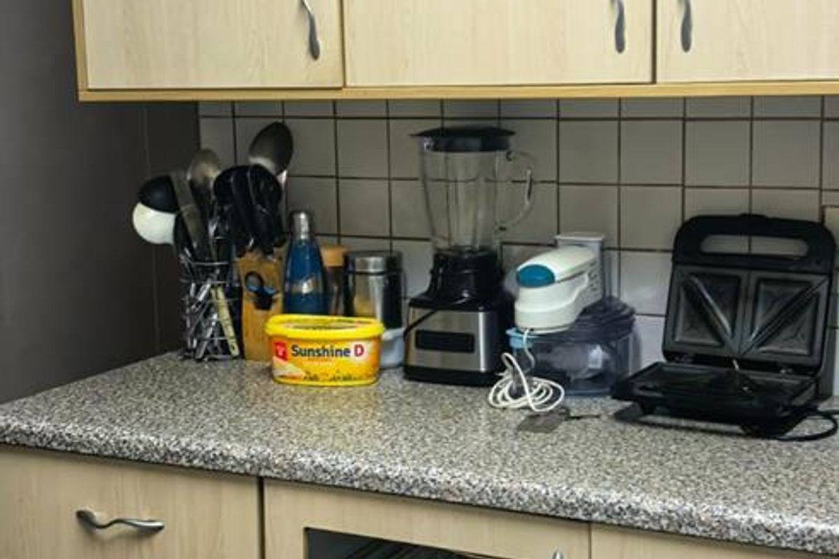 A kitchen section featuring light wood-tone cabinetry, a granite-look countertop, and a tiled backsplash, currently showing a missing cabinet door panel.