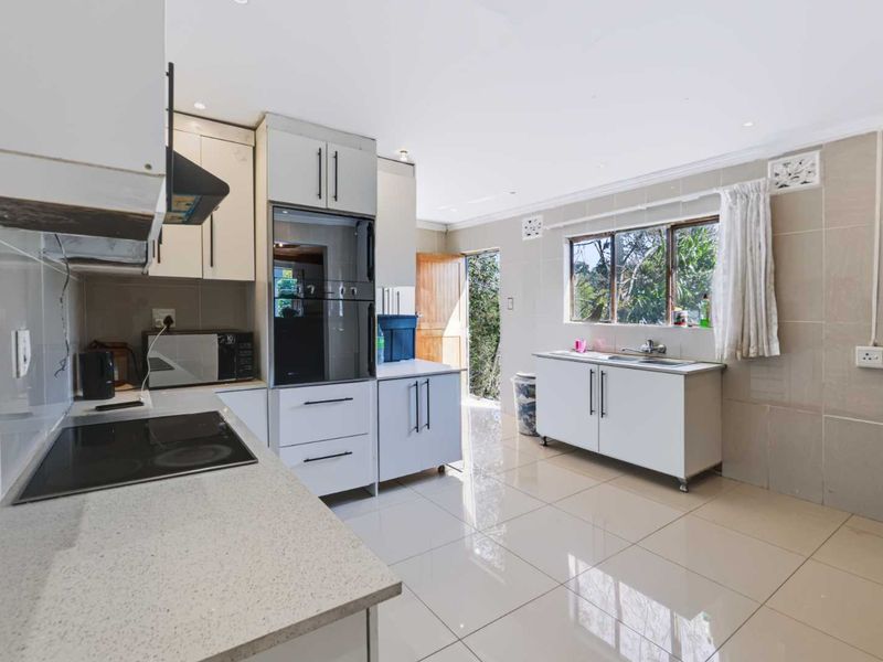 A functional kitchen featuring white cabinetry, stone countertops, integrated oven and hob, tiled flooring, and direct access to the exterior.