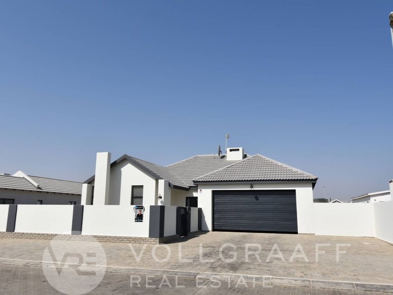 Modern single-story residential home featuring a tiled roof, paved driveway, and a secure double garage with a perimeter wall.