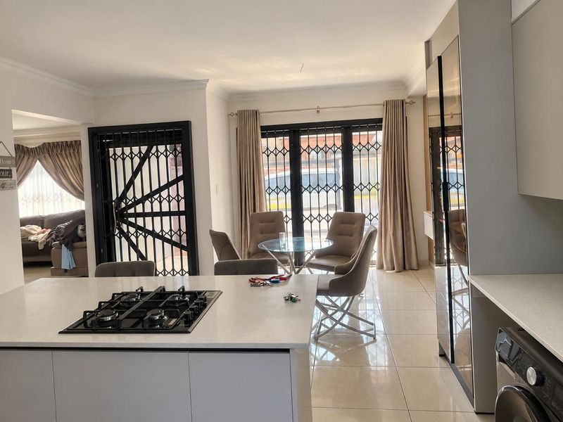 Modern open-plan kitchen and dining area featuring a central island with gas hob, sleek cabinetry, and tiled flooring with access to the exterior.