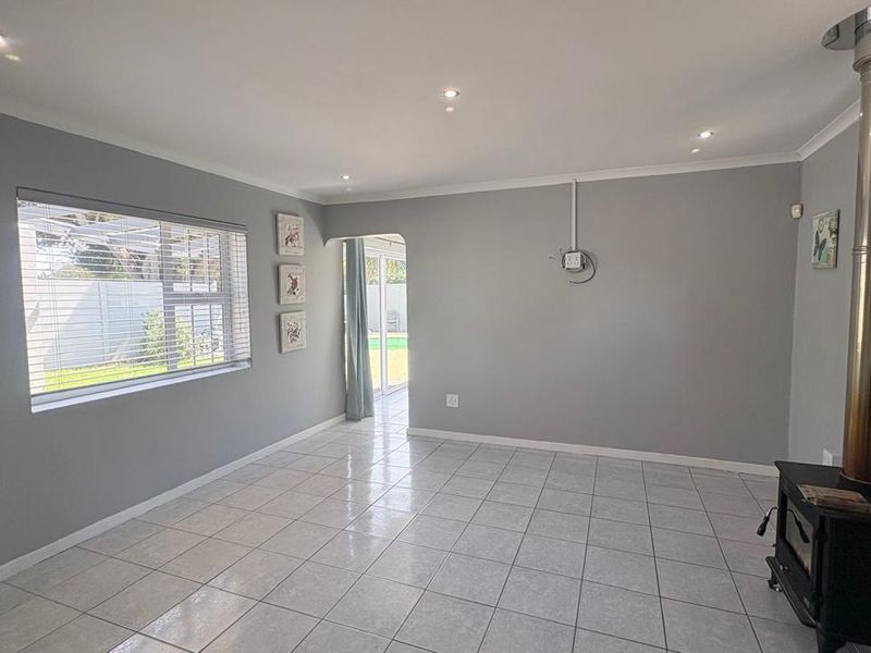 Spacious living area featuring neutral grey walls, tiled flooring, recessed lighting, and a built-in wood-burning fireplace, with direct access to the rear garden.