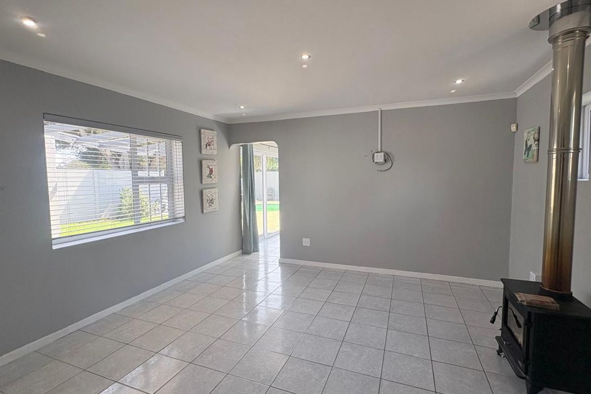 Spacious living area featuring neutral grey walls, tiled flooring, recessed lighting, and a built-in wood-burning fireplace, with direct access to the rear garden.