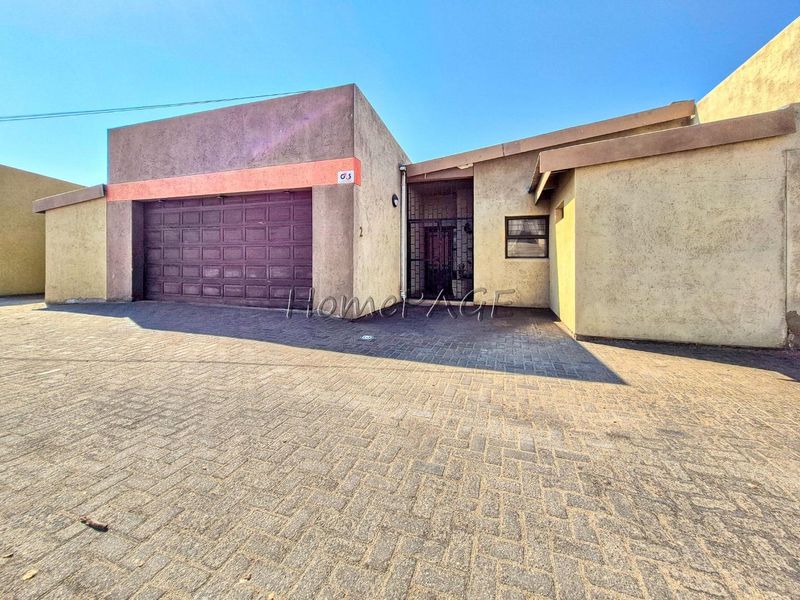 Front elevation of the property featuring a single garage, paved driveway, and secure entrance gate with a textured stucco facade.