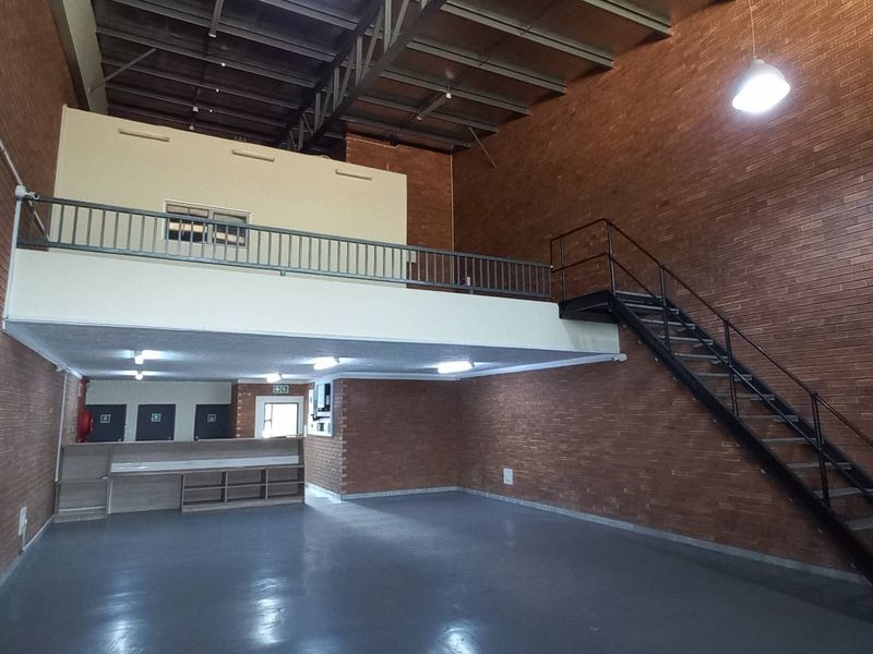 Spacious industrial unit featuring exposed brick walls, a mezzanine level with metal railing, and a dedicated staircase, suitable for various commercial or storage uses.