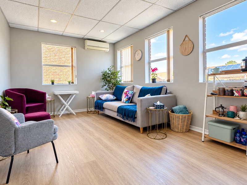 A bright and well-maintained office space featuring laminate flooring, a suspended ceiling with recessed lighting, and a wall-mounted air conditioning unit.