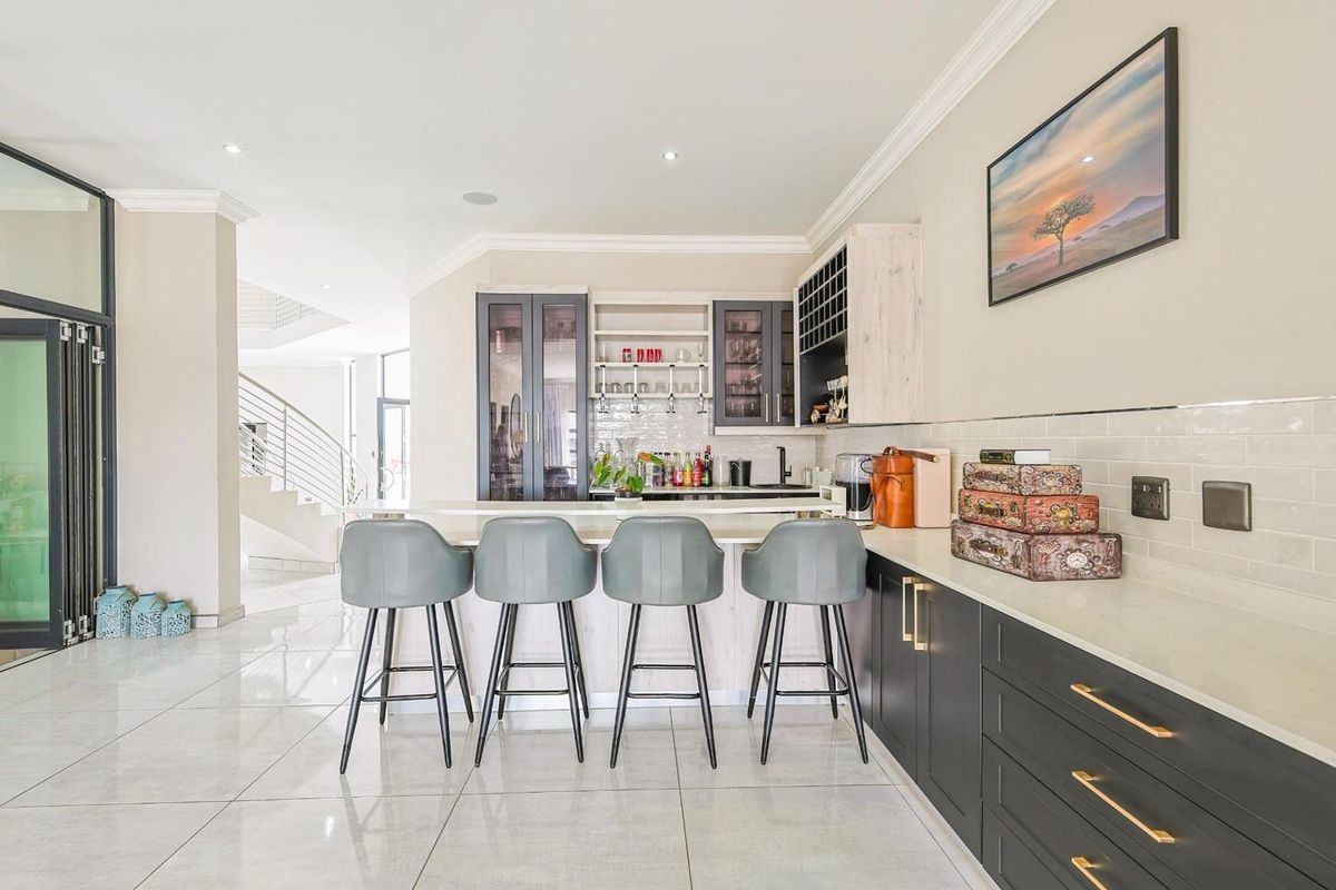 Modern kitchen featuring sleek dark cabinetry, stone countertops, a breakfast bar, and integrated shelving, seamlessly flowing into the open-plan living area.