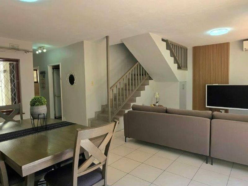 Open-plan living and dining area featuring tiled flooring, a central staircase with balustrade, and a decorative slatted wood feature wall.