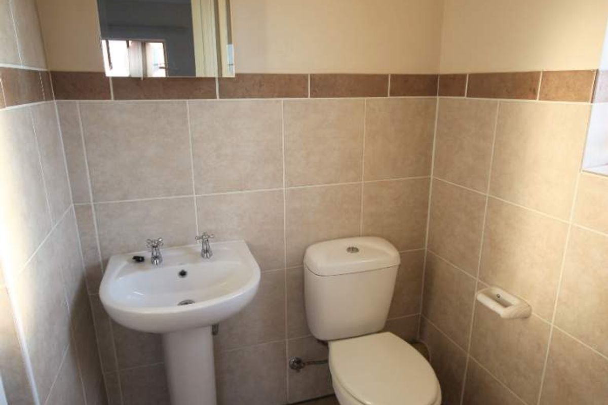 A functional bathroom featuring a pedestal basin, toilet, and neutral ceramic wall and floor tiling with a decorative border.