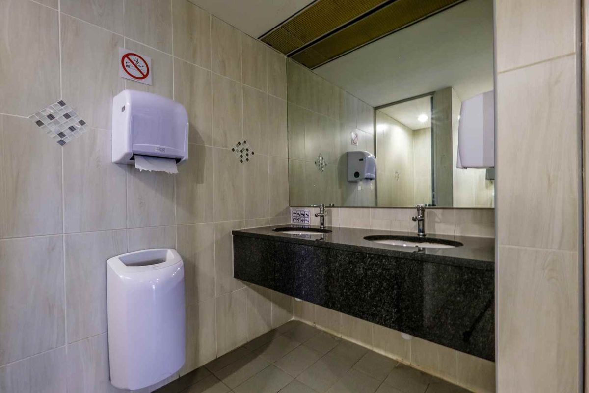 A clean, functional commercial bathroom featuring a double vanity with granite countertops, under-mount sinks, and large wall-mounted mirrors.