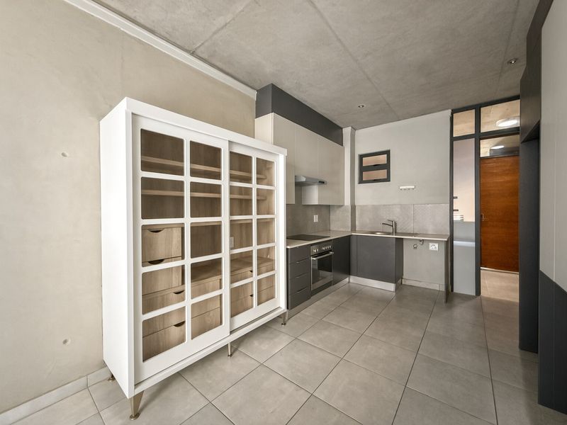 Modern kitchen featuring sleek cabinetry, built-in oven and hob, stainless steel sink, and contemporary tiled flooring with an industrial exposed concrete ceiling.
