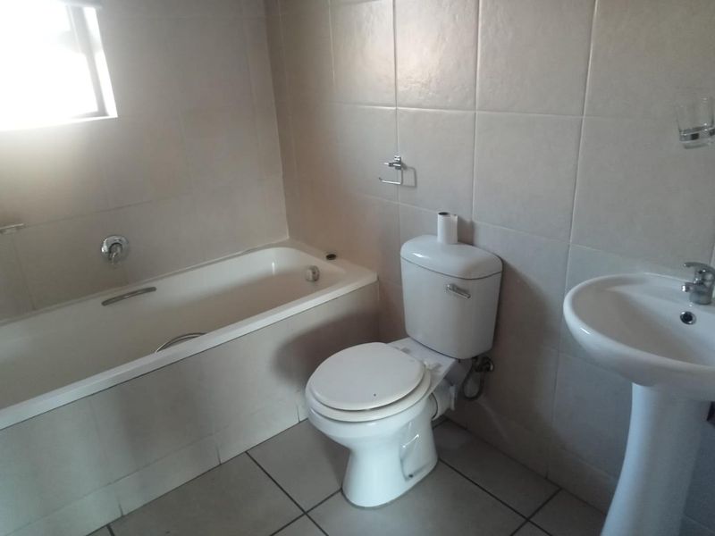 A functional bathroom featuring a standard bathtub, pedestal basin, and toilet with neutral wall and floor tiling.