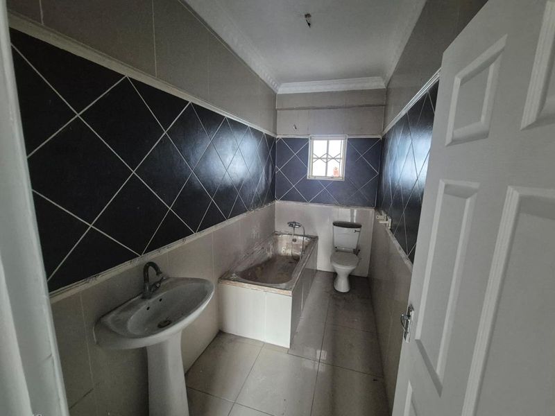 A dated bathroom featuring a pedestal basin, built-in bathtub, and toilet, finished with dark and light ceramic wall tiling.