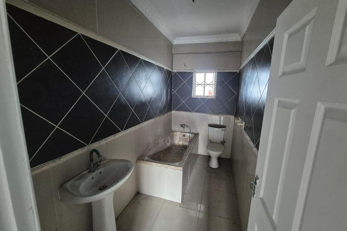 A dated bathroom featuring a pedestal basin, built-in bathtub, and toilet, finished with dark and light ceramic wall tiling.