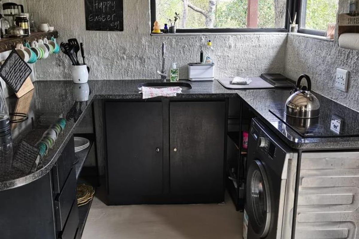 Compact kitchen featuring dark cabinetry, granite countertops, and corner windows with a rustic textured wall finish.