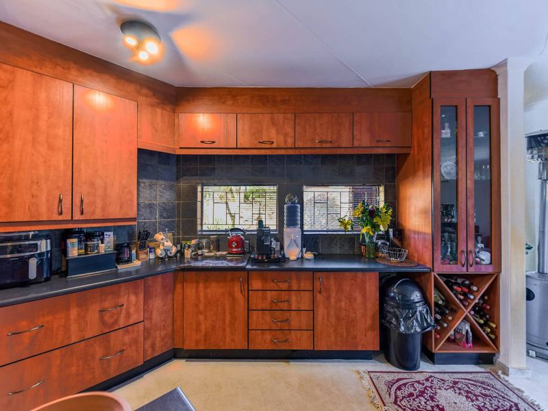 A functional kitchen featuring warm-toned wooden cabinetry, dark laminate countertops, a tiled backsplash, and a dedicated built-in wine storage rack.