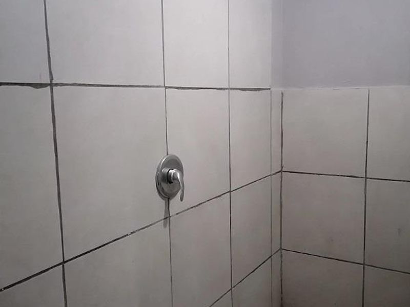 A functional shower area featuring wall-mounted shower fixtures, tiled walls, and tiled flooring in need of maintenance.