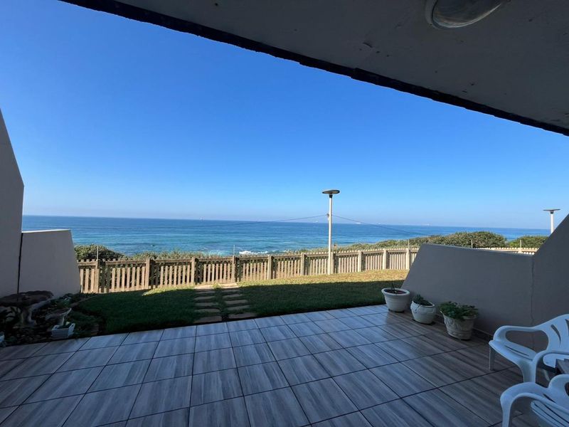 A covered patio area featuring tiled flooring and a direct view of the ocean, providing a seamless transition to the outdoor garden space.