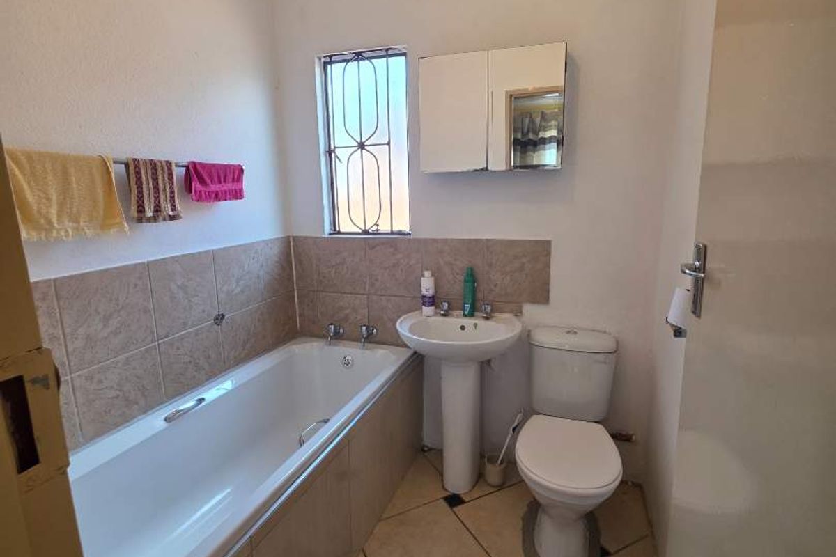 A functional bathroom featuring a built-in bathtub, pedestal basin, toilet, and wall-mounted medicine cabinet with tiled splashbacks.