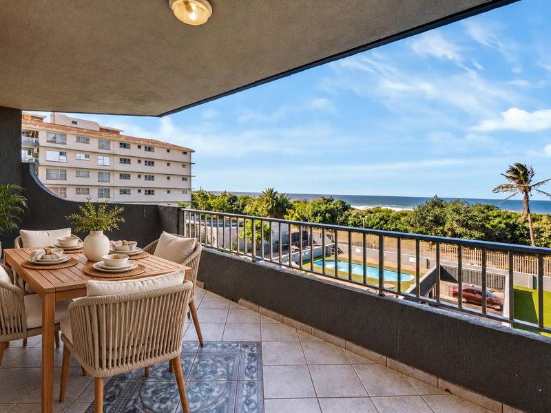 Spacious covered balcony featuring tiled flooring, a secure metal balustrade, and scenic views overlooking the complex pool and ocean.