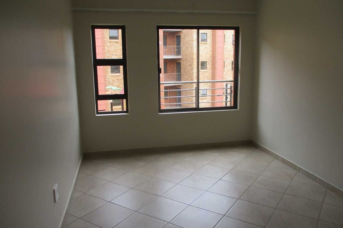 An empty bedroom featuring neutral wall paint, tiled flooring, and aluminium-framed windows overlooking the apartment complex.