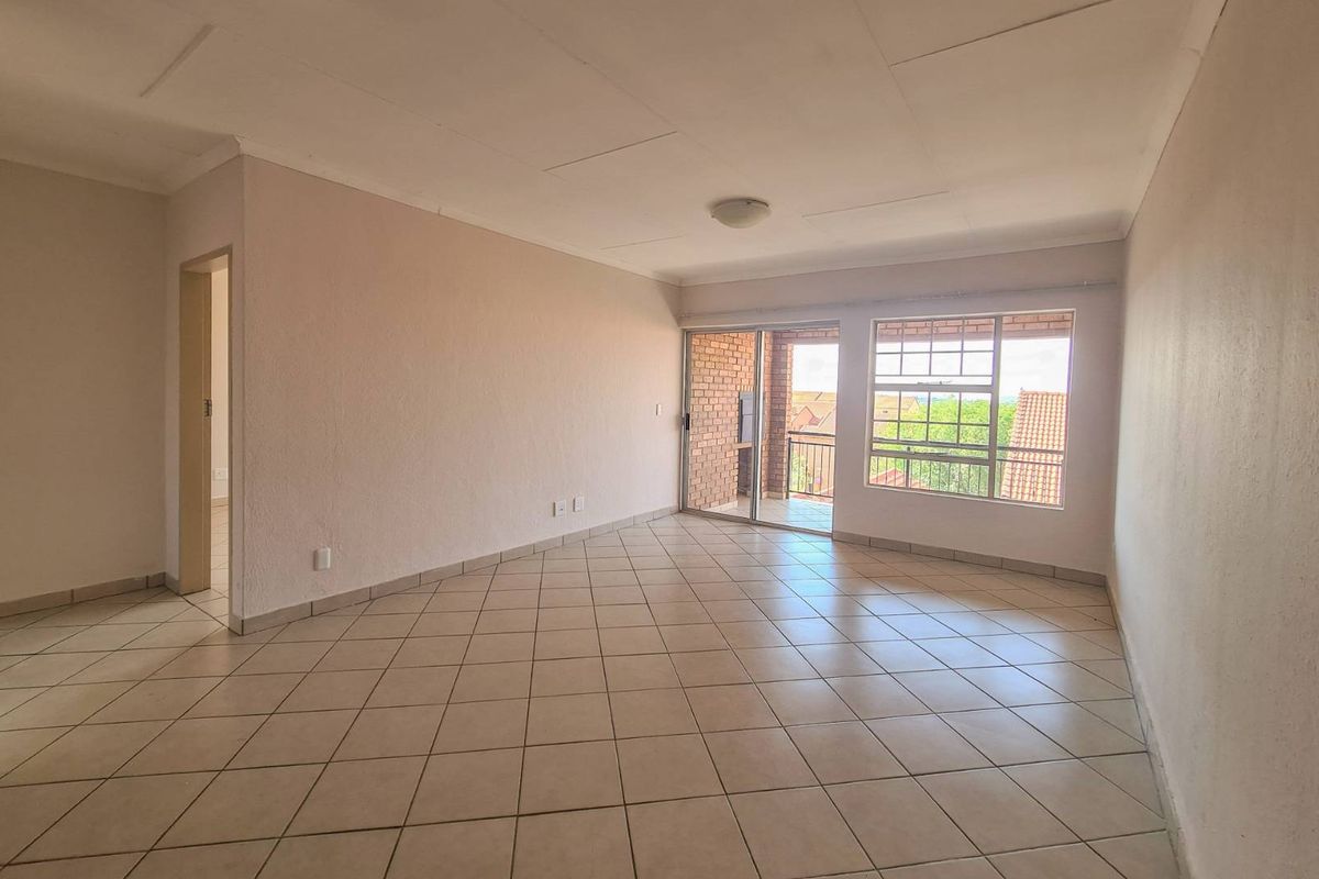 Spacious, empty living area featuring neutral tiled flooring, natural light from large windows, and access to an outdoor balcony.
