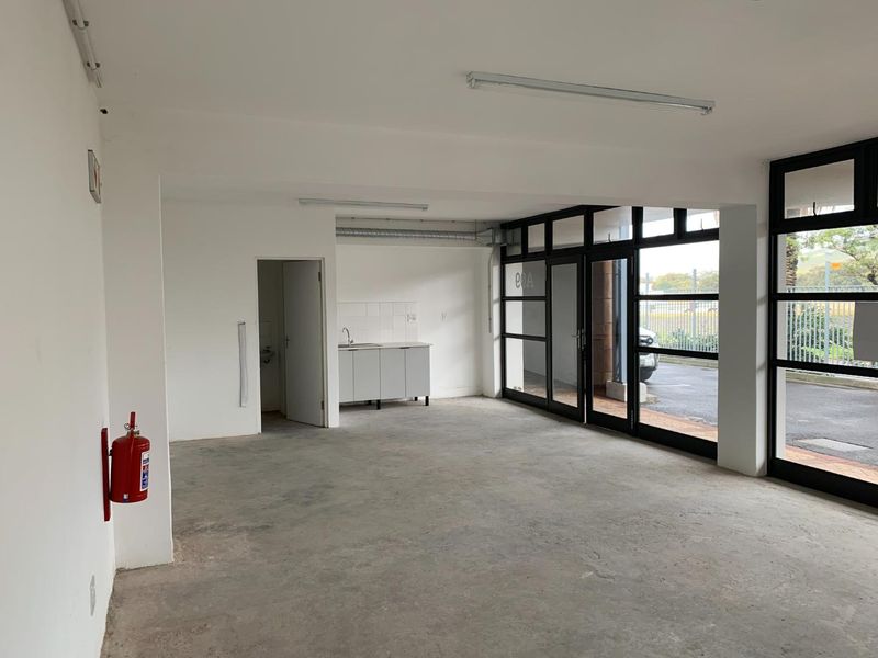An open-plan commercial or mixed-use space featuring concrete flooring, a small kitchenette area, and large glass doors providing natural light and exterior access.