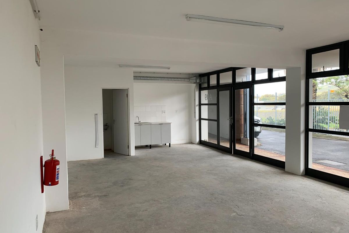 An open-plan commercial or mixed-use space featuring concrete flooring, a small kitchenette area, and large glass doors providing natural light and exterior access.