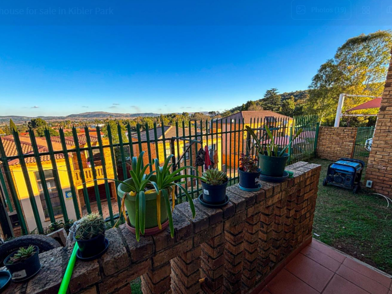 An elevated brick balcony featuring a tiled floor and metal fencing, offering expansive views of the surrounding neighborhood and landscape.