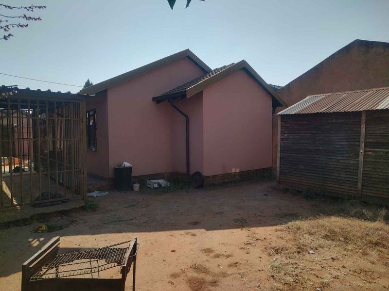 Rear view of the property showing the exterior wall, tiled roof, metal security gate, and a detached timber storage shed on unpaved ground.