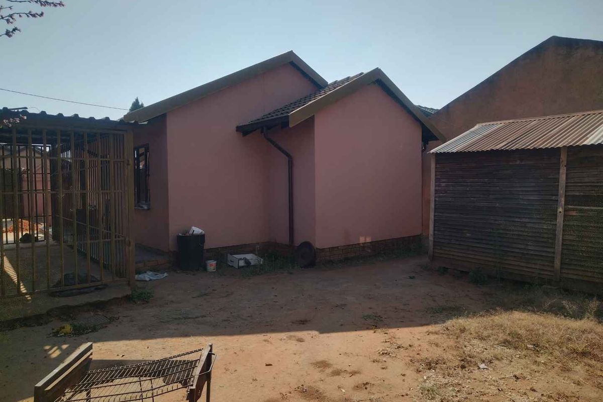 Rear view of the property showing the exterior wall, tiled roof, metal security gate, and a detached timber storage shed on unpaved ground.