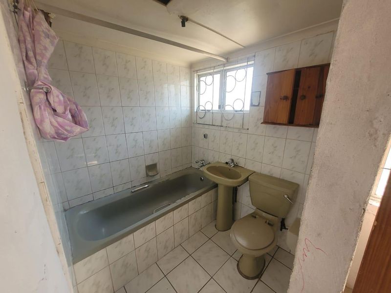 A dated bathroom featuring a bathtub, pedestal basin, and toilet, with wall and floor tiling. The space requires renovation and modernization of fixtures.