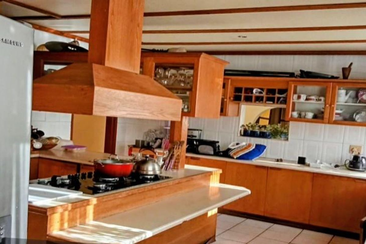 Spacious kitchen featuring extensive wooden cabinetry, a central island with a built-in hob and extractor fan, and tiled flooring.