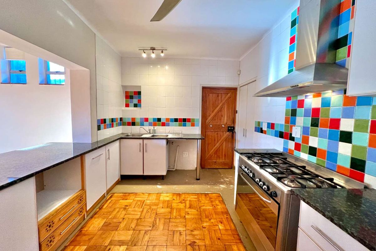 A functional kitchen featuring parquet flooring, a gas stove with stainless steel extractor, and a colorful tiled splashback with ample built-in cabinetry.