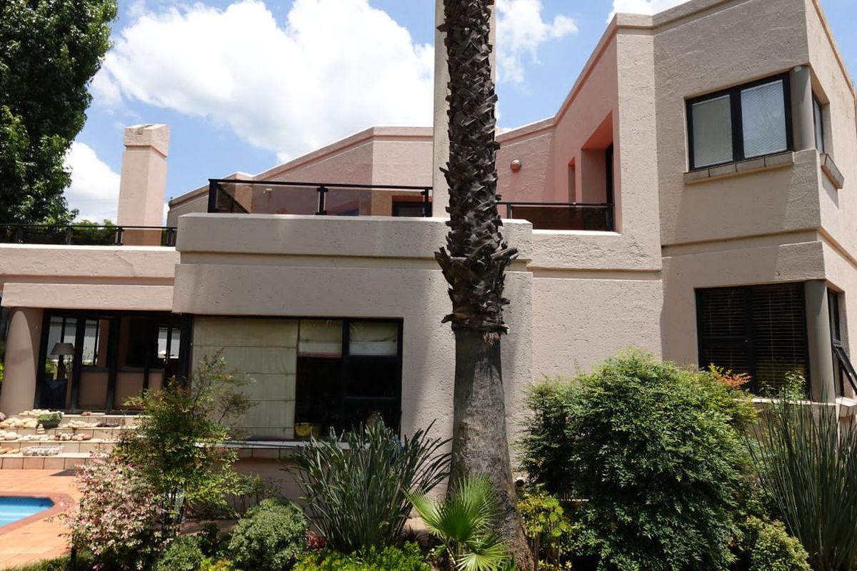 Rear view of the house featuring a swimming pool, a raised patio area with glass balustrades, and established garden landscaping.