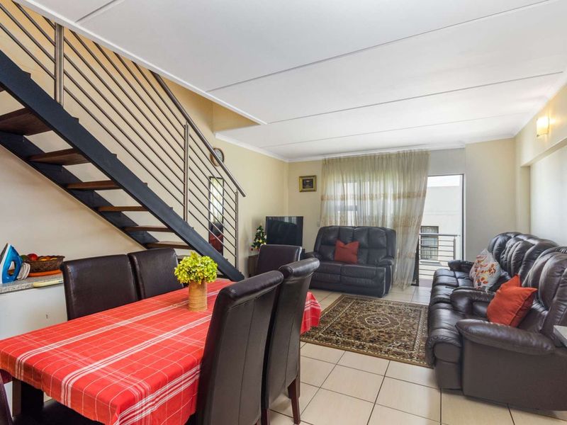 Open-plan living and dining area featuring tiled floors, a modern metal staircase, and direct access to a balcony through a sliding door.