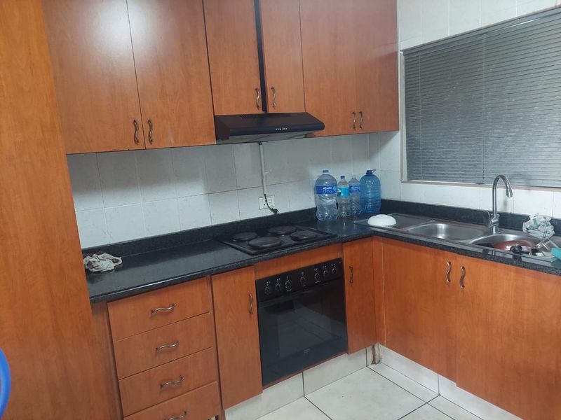 A functional kitchen featuring wooden cabinetry, granite countertops, a built-in oven with hob, and a double sink with tiled backsplash.