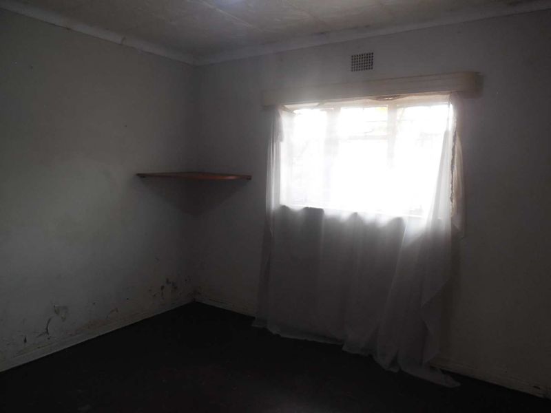 An empty bedroom featuring a built-in corner shelf and ceiling vent, showing significant signs of wall surface deterioration and damp staining.