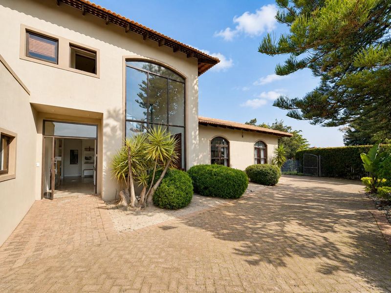 Front elevation of a well-maintained house featuring a paved driveway, large arched windows, and a classic terracotta tiled roof.