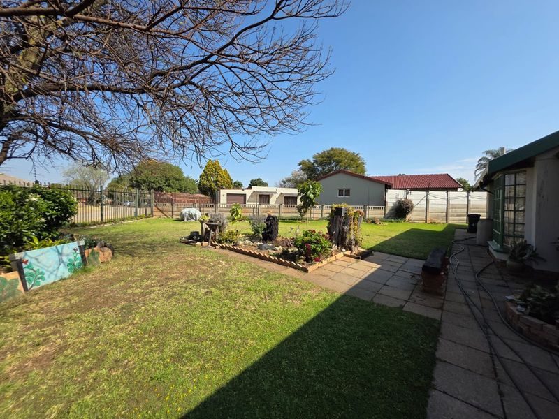 A spacious rear garden featuring a paved walkway, established lawn, and secure perimeter fencing, offering a private outdoor area.