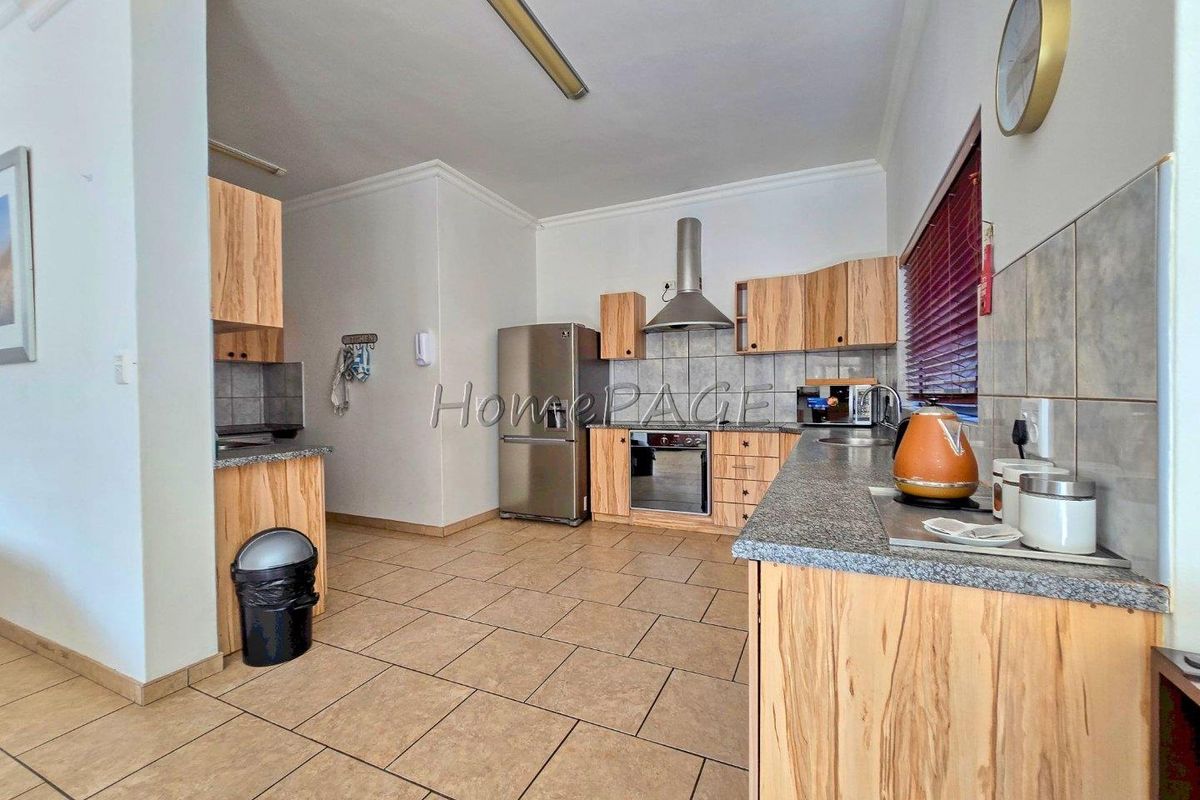 Functional kitchen featuring light wood-grain cabinetry, granite countertops, tiled splashbacks, and stainless steel built-in oven with extractor fan.