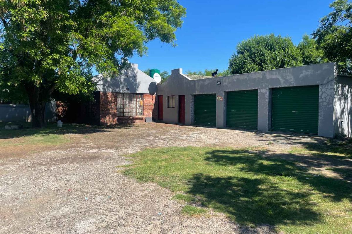 Front view of a small holding property featuring a triple garage with roll-up doors, brick facade detailing, and a large paved driveway area.