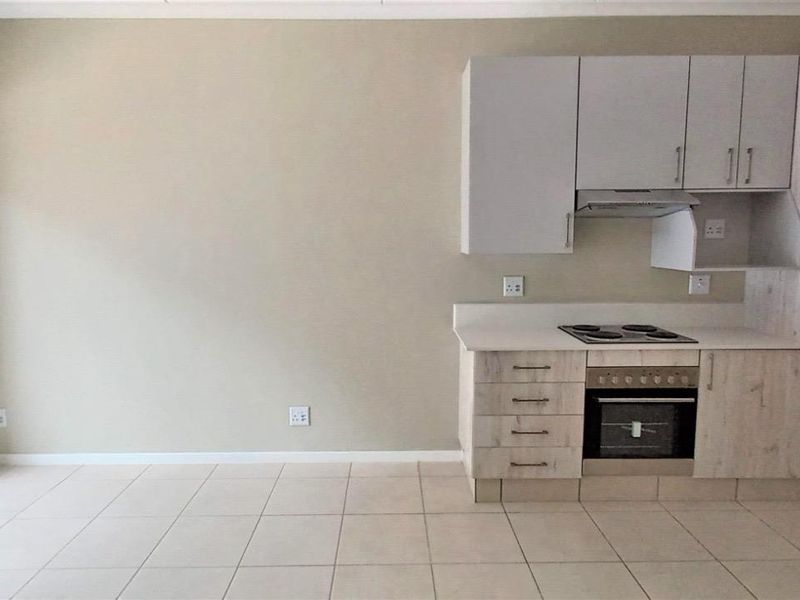 Open-plan kitchen and living area featuring light wood-finish cabinetry, built-in oven and hob, tiled floors, and access to a balcony through a sliding door.