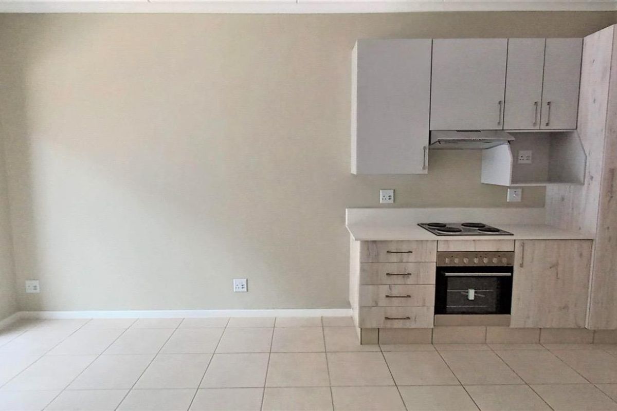 Open-plan kitchen and living area featuring light wood-finish cabinetry, built-in oven and hob, tiled floors, and access to a balcony through a sliding door.