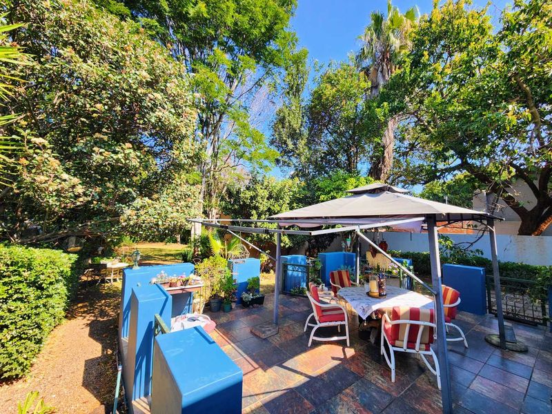 A paved outdoor patio area featuring low blue masonry walls, surrounded by a mature, leafy garden setting.
