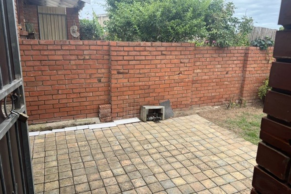 A private rear courtyard featuring a paved patio area enclosed by a solid brick boundary wall, offering potential for outdoor landscaping and improvement.