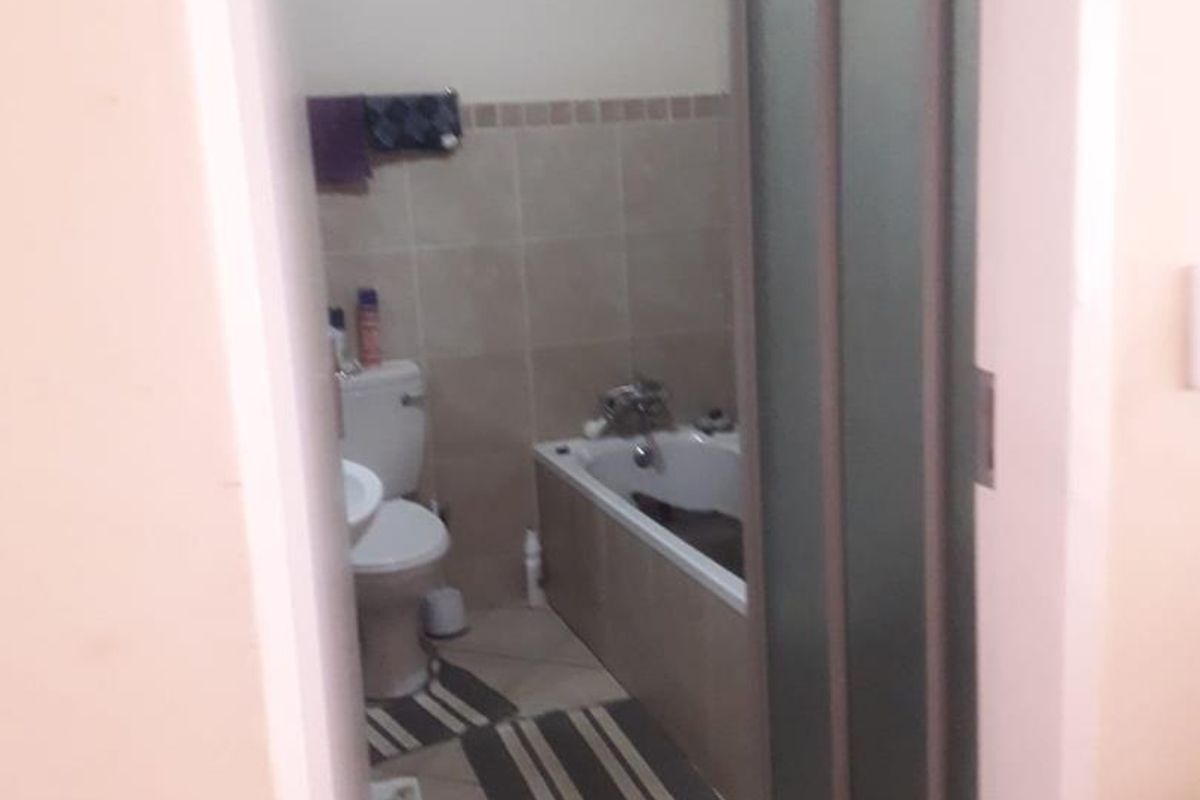 A functional bathroom featuring a bathtub with shower screen, toilet, and pedestal basin with tiled flooring and wall accents.