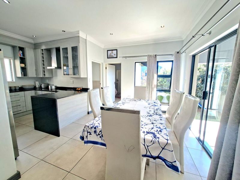 Open-plan kitchen and dining area featuring modern cabinetry, granite countertops, tiled flooring, and large sliding doors providing access to the outdoor space.