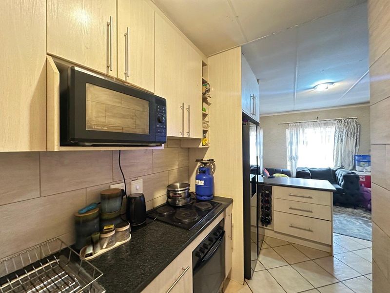 Open-plan kitchen featuring light wood cabinetry, dark stone countertops, built-in oven and hob, flowing into a connected living area with tiled flooring.